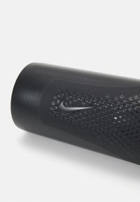 Zwart Nike-product met een gestructureerde grip, met een geometrisch patroon en een klein logo. Strakke cilindervorm, gladde en matte afwerking.