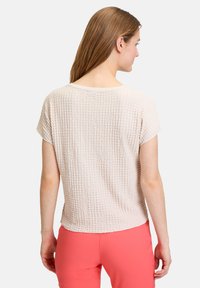 Light pink, textured knit top with short sleeves, round neckline, and relaxed fit. Waffle pattern adds visual interest to the design.