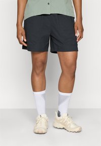 Sorte shorts med en glat tekstur, der har frontlommer og en afslappet pasform, sammen med hvide sokker og lysebeige træningssko.