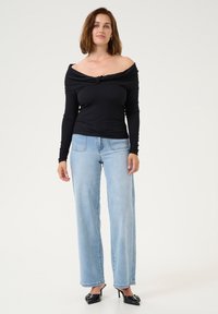 Black off-the-shoulder ribbed top with long sleeves, knotted detail at the front, paired with light blue wide-leg jeans and black heels.