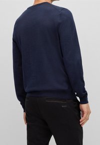 Pull bleu marine en tissu maille doux, avec un col rond et des manches longues, associé à un pantalon noir ajusté.
