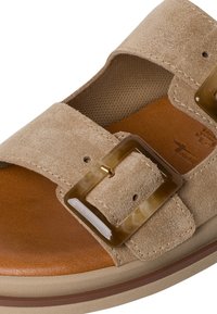Beige suede sandal with a brown leather footbed, wide strap, and a marbled buckle detail. Durable sole with brown accent band.