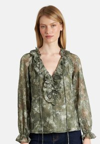 Durchsichtige grüne Bluse mit Blumenmuster, Rüsche am Halsauschnitt und langen Ärmeln. Verfügt über Kordelzüge und geraffte Manschetten. Strukturierter Stoff.