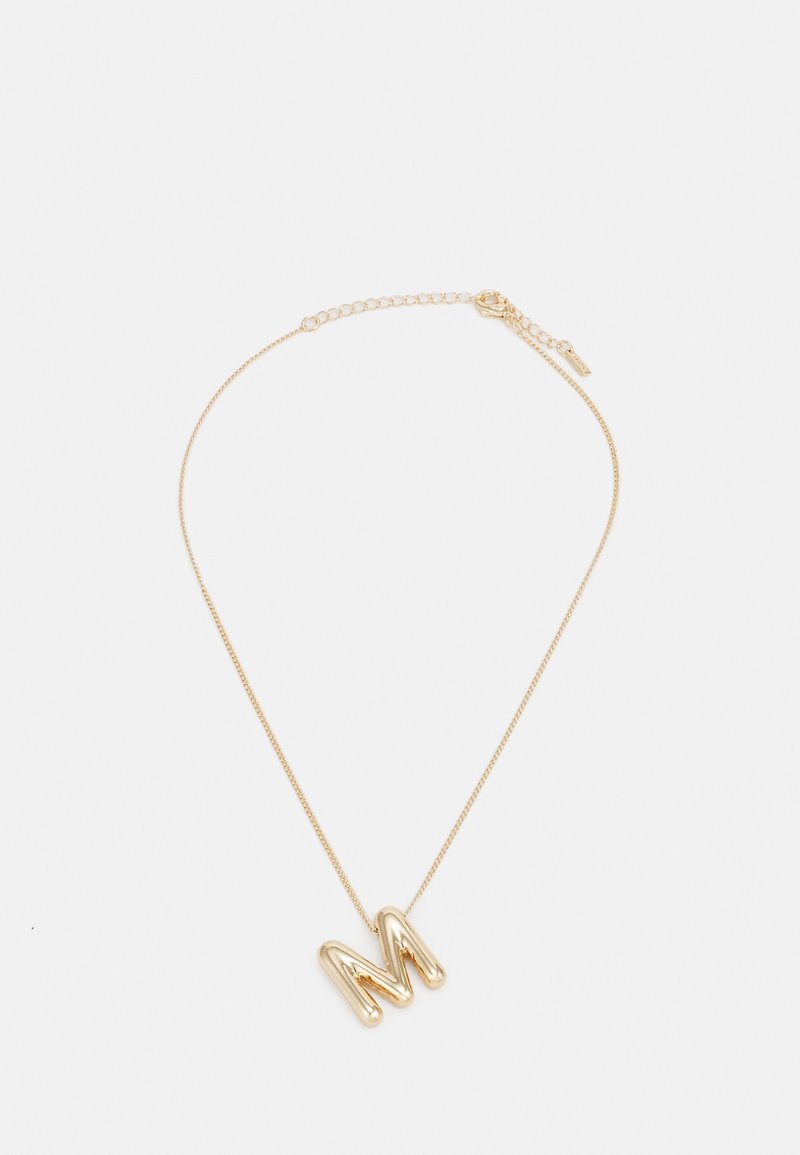 Collier délicat en chaîne d'or avec un grand pendentif en forme de lettre "M" dorée brillante et fermoir ajustable sur fond blanc.