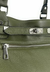 Sac à main en cuir texturé vert avec une fermeture éclair en argent et un fermoir à verrou tournant, montrant des poignées fixées par des anneaux en métal.