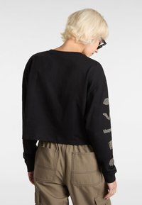 Zwart cropped sweatshirt met lange mouwen en grafische details op de mouwen, gecombineerd met olijfgroene cargobroek met grote opgestikte zakken.