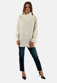 Overmaat wit sweater met een col, geribbelde manchetten en zoom, gecombineerd met donkerblauwe jeans en zwarte puntige hakken. Vezelachtige textuur.