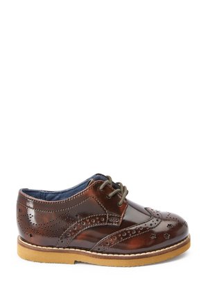 Chaussure brogue en cuir marron avec motifs perforés d'étoiles et de points, semelle beige et lacets vert foncé, vue de côté.