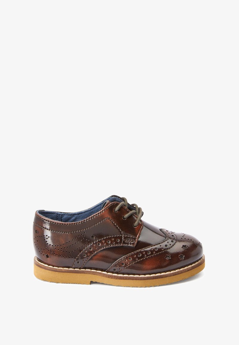 Chaussure brogue en cuir marron avec motifs perforés d'étoiles et de points, semelle beige et lacets vert foncé, vue de côté.