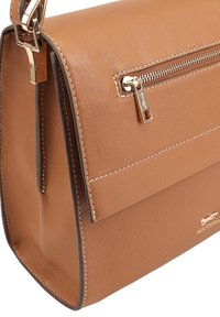 Tan leren handtas met een gestructureerde vorm, voorzien van een ritsvak, contrasterende stitching en een gouden logo-accent aan de zijkant.