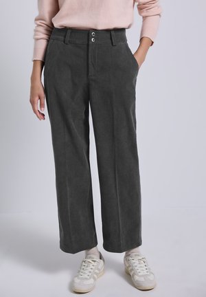 Grijze corduroy wijdlopende broek met twee voorzakken en sluiting met twee knopen. Gecombineerd met lichtgekleurde sneakers voor contrast.