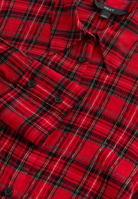 Rotes kariertes Hemd mit strukturiertem Muster, schwarzen Knöpfen, einem Kragen und verschiedenen Schattierungen von Rot, Grün und Schwarz im gesamten Stoff.