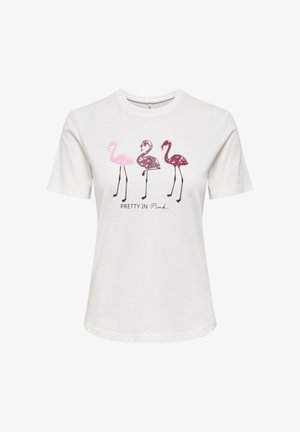 Mujer con blazer de ante marrón sobre camiseta blanca con estampado de flamencos, vaqueros azul claro, cinturón marrón y zapatos negros, de pie contra un fondo liso.