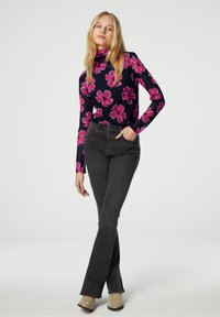 Langdurige turtleneck met marineblauwe stof met een groot roze bloemenpatroon, gecombineerd met hoge zwarte jeans en beige enkellaarsjes.