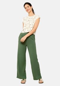 Lace-patterned cream top with short sleeves, paired with loose-fitting green pants. Shoes are gold with a cork accent. Simple, casual look.