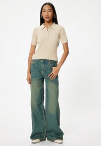 Beige geribbelde polo met korte mouwen en een kraag, gecombineerd met loszittende vervaagde teal jeans en witte schoenen.