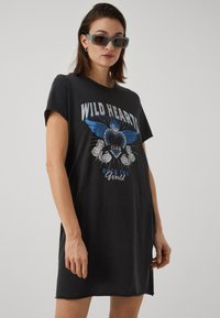 Črna prevelika majica obleka s tiskom "WILD HEARTS CLUB" v modri in beli barvi, ki vsebuje motiv ptice z krili in vrtnico. Kratke rokave, ohlapen kroj.