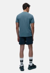 Menns kortermet t-skjorte i teal, kombinert med mørke shortser. Har rund hals og en jevn tekstur. Bærers med hvite sokker og svarte joggesko.