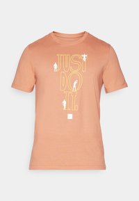 Oranje katoenen t-shirt met "JUST DO IT" in grote gele tekst en kleine witte figuren. Korte mouwen en een ronde halsontwerp.