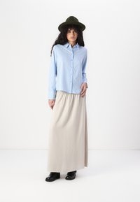 Light blue and white striped button-up shirt, cream maxi skirt, black boots, and an olive-green wide-brim hat.