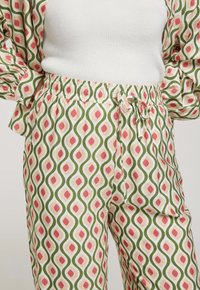 Pantalons à motifs avec une taille élastique réglable, présentant un design de lignes ondulées en vert, pêche et crème, fabriqués en tissu léger.