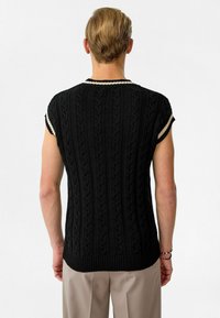 Zwart gebreid mouwloos topje met een kabelpatroon, ribbelige zoom en contrasterende off-white afwerking op de mouwen en de halslijn.