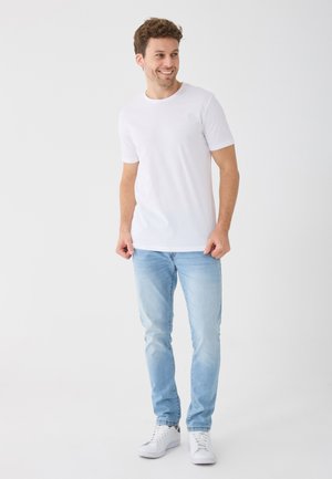 White short-sleeve t-shirt paired with light blue jeans and white sneakers. The jeans feature a slight fade, providing a casual look.