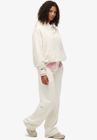 Oversized hættetrøje i cremefarve med frontlomme, kombineret med en lyserød stribet skjorte under og matchende sweatpants. Tekstureret stof, afslappet pasform.