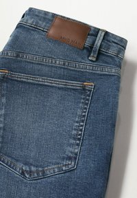 Zone de la poche arrière d'un jean en denim bleu plié avec couture visible et une étiquette de marque en cuir marron sur la ceinture.