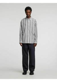 Stripete skjorte med knapper i svart og hvitt, med klassisk krage og brystlomme. Kombinert med marineblå bukser og svarte sko.