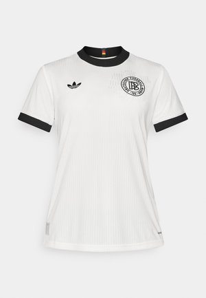Personne portant un maillot de sport blanc à manches courtes avec col et poignets noirs, et un short noir avec petits logos Adidas.