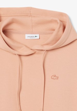 Avslappnad passform hoodie i ljus persikofärg, tillverkad av mjukt tyg. Har en känguruficka och broderad Lacoste-logga på bröstet.