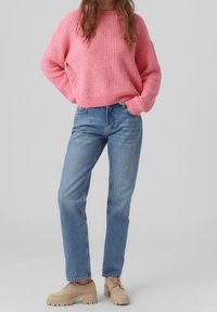 Rosa strukturiertes Strickoberteil mit lockerer Passform, kombiniert mit hellblauen geraden Jeans und beigen Schnürschuhen mit robuster Sohle.