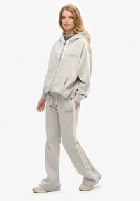 Light gray hoodie and sweatpants set, fleece material, relaxed fit, white side stripes, front pocket, zip front, minimal branding.