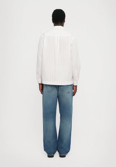 Chemise à rayures à manches longues blanche et rouge, associée à un jean en denim bleu à jambes larges, mettant en avant une coupe décontractée et un design de poche classique.