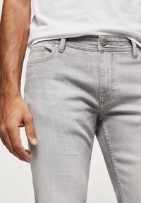 Jeans de denim gris claro con un corte slim, diseño de cinco bolsillos y costuras en contraste. Presentan un cierre de botón y trabillas para el cinturón.