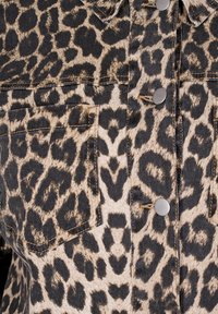 Camisa de denim con un estampado de leopardo en beige y negro, botones en tono plateado y bolsillos estructurados. Tejido ligeramente texturizado.
