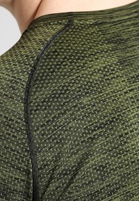 Grön atletisk tröja med ett texturerat mönster av mörkgrön och svart. En slät, figurnära design med synliga sömnadsdetaljer.