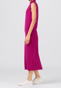 Fuchsia ärmlös topp med hög halsringning, matchad med en knälång kjol. Modellen bär vita sneakers. Slät tygkvalitet.