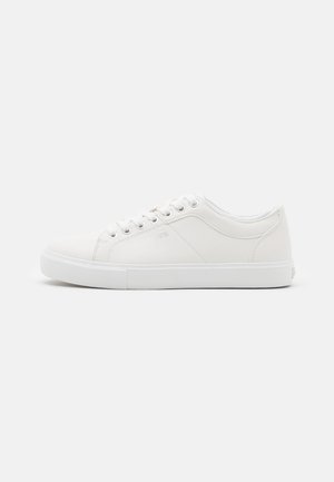White sneakers made of smooth synthetic material, featuring round toe, low top, flat white sole, and six eyelet lace-ups. Minimalist design.