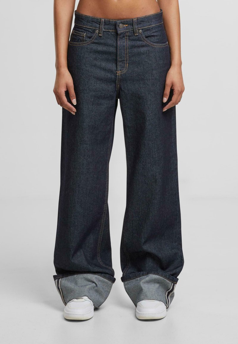 Plačios džinsinės kelnės tamsiu skalbimu, su kontrastingomis oranžinėmis siūlėmis ir laisvu kirpimu. Akcentai: sukrautas kraštas ir šoninės kišenės.