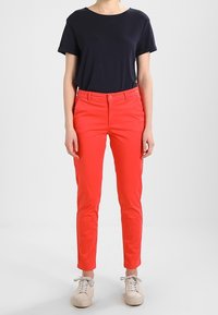 Červené bavlněné kalhoty se slim fit a předními kapsami, doplněné námořnickou modrou krátkým rukávem. Bílé tenisky dokončují outfit.