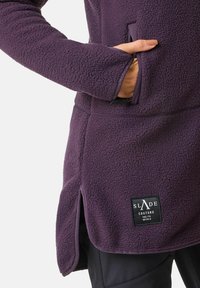 Lila Fleecejacke aus strukturiertem Stoff, mit Seitentaschen und einem Logopatch an der unteren Vorderseite. Verfügt über einen gebogenen Saum und lange Ärmel.