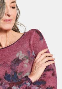 Lange mouwen sweater van een zachte, lichte stof met een bloemenpatroon in paarse, roze en groene tinten; bootnek ontwerp.