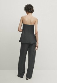 Top peplum noir sans manches avec une coupe droite, associé à un pantalon à jambes larges. Texture lisse et finition mate sur les deux pièces.