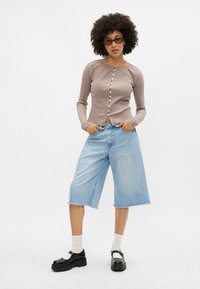 Top cu mânecă lungă, côtelat, de culoare bej deschis, cu închidere cu nasturi; asortat cu șorturi din denim lejere, până la genunchi, de culoare albastră deschisă și pantofi cu platformă negri.
