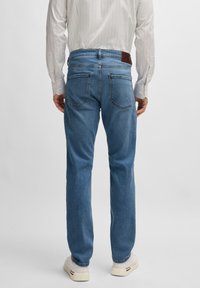 Light blue straight-leg jeans with five pockets, denim fabric, faded finish, and brown leather patch at the waistband. Worn with a striped shirt.