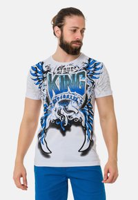 Weißes T-Shirt mit kurzen Ärmeln, das ein blaues und schwarzes Grafikdesign mit Flügeln und dem Text "TRUE KING" zeigt. Das Material wirkt weich und leicht.