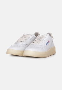 Sneaker in pelle bianca con suole in gomma beige, punta rotonda e design perforato. Presentano lacci beige e un logo sul lato.