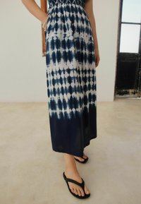 Blå och vit tie-dye maxi klänning med elastisk midja och fickor, kombinerad med svarta flip-flops. Slät tyg med en flödande design.